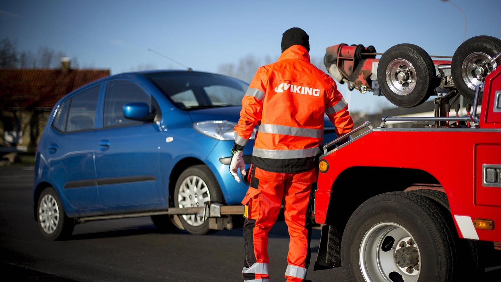 Hinausauton kuljettaja oranssissa univormussa ja heijastavassa liivissä lastaa sinisen auton punaiseen Viking-hinausautoon.