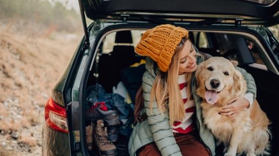 Smilende kvinde sidder på bagsædet af en bil med en hund ved siden af sig.