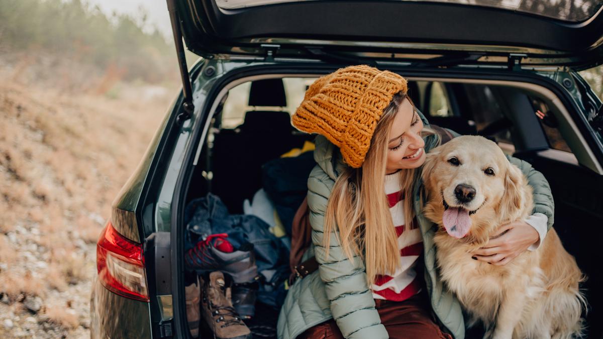 Smilende kvinde sidder på bagsædet af en bil med en hund ved siden af sig.