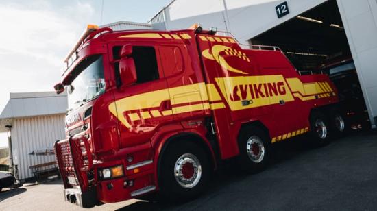 Suuri punainen ja keltainen hinausauto, jossa lukee "VIKING", on pysäköity autotallin ulkopuolelle, jossa on numero 12.