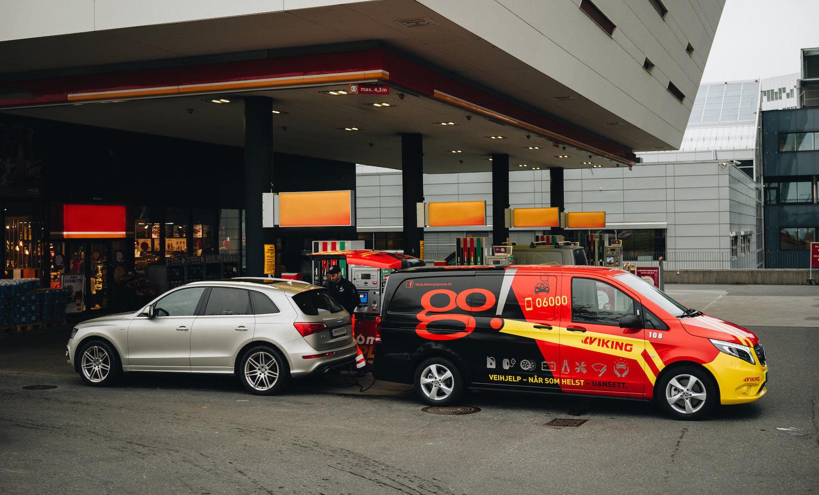 Viking roadside assistance car drains the fuel tank of a silver station wagon at a service station.
