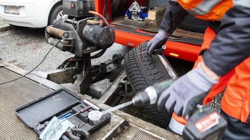 Vikingin tiepalvelun työntekijä työskentelee auton renkaan parissa sähkötyökalulla, taustalla erilaisia työkaluja ja rengas.