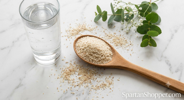 Psyllium husk powder in wooden spoon with glass of water on white marble