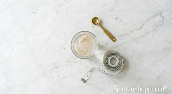 Psyllium husk powder mixed in a glass of water next to a measuring tape on a white marble surface