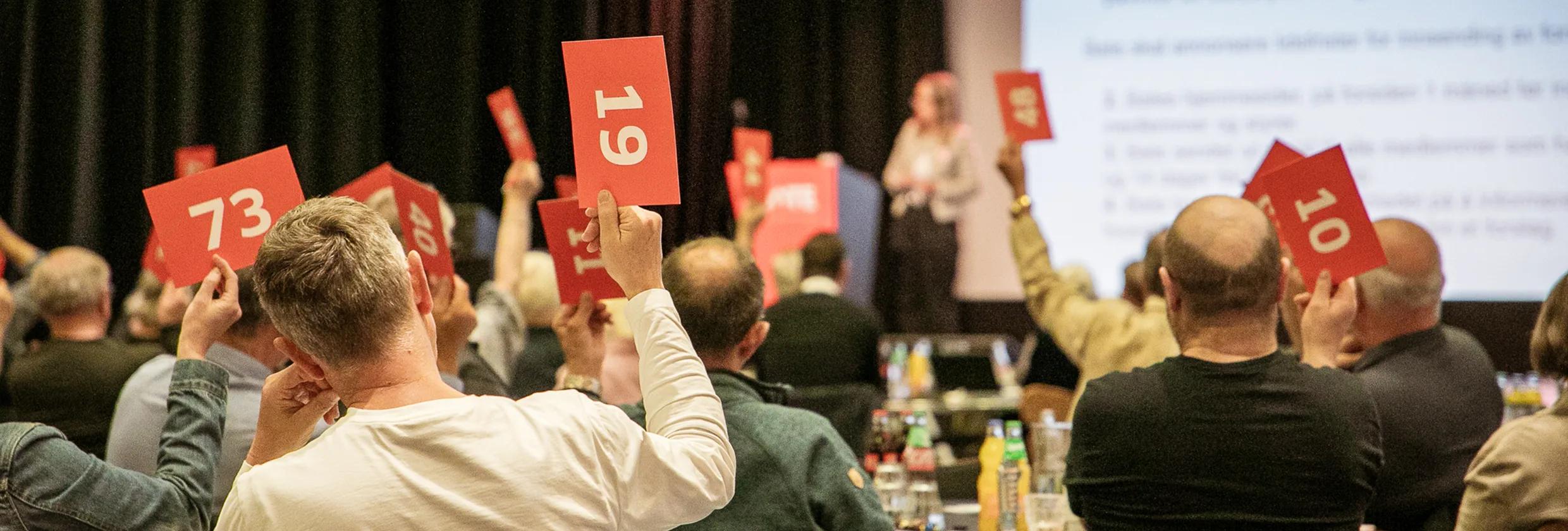 Personer rekker opp stemmeseddel på generalforsamling.