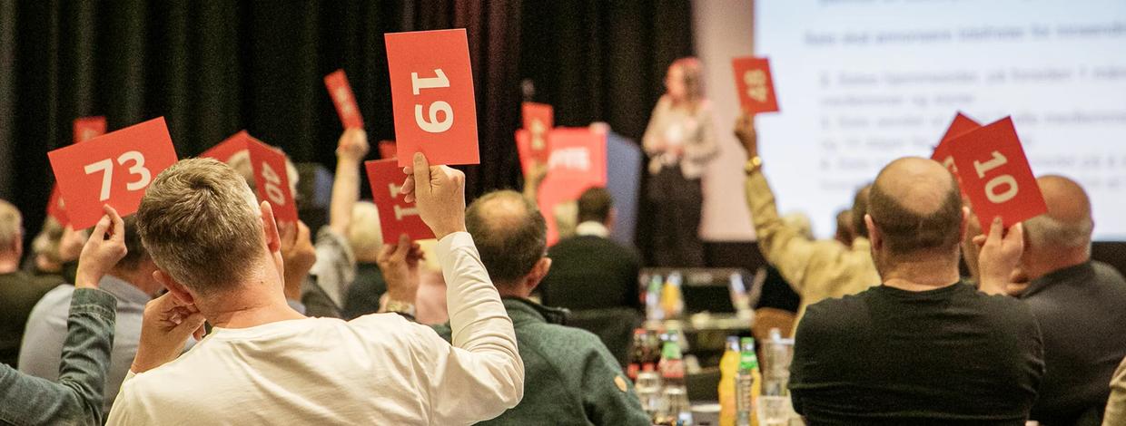 Personer rekker opp stemmeseddel på generalforsamling.