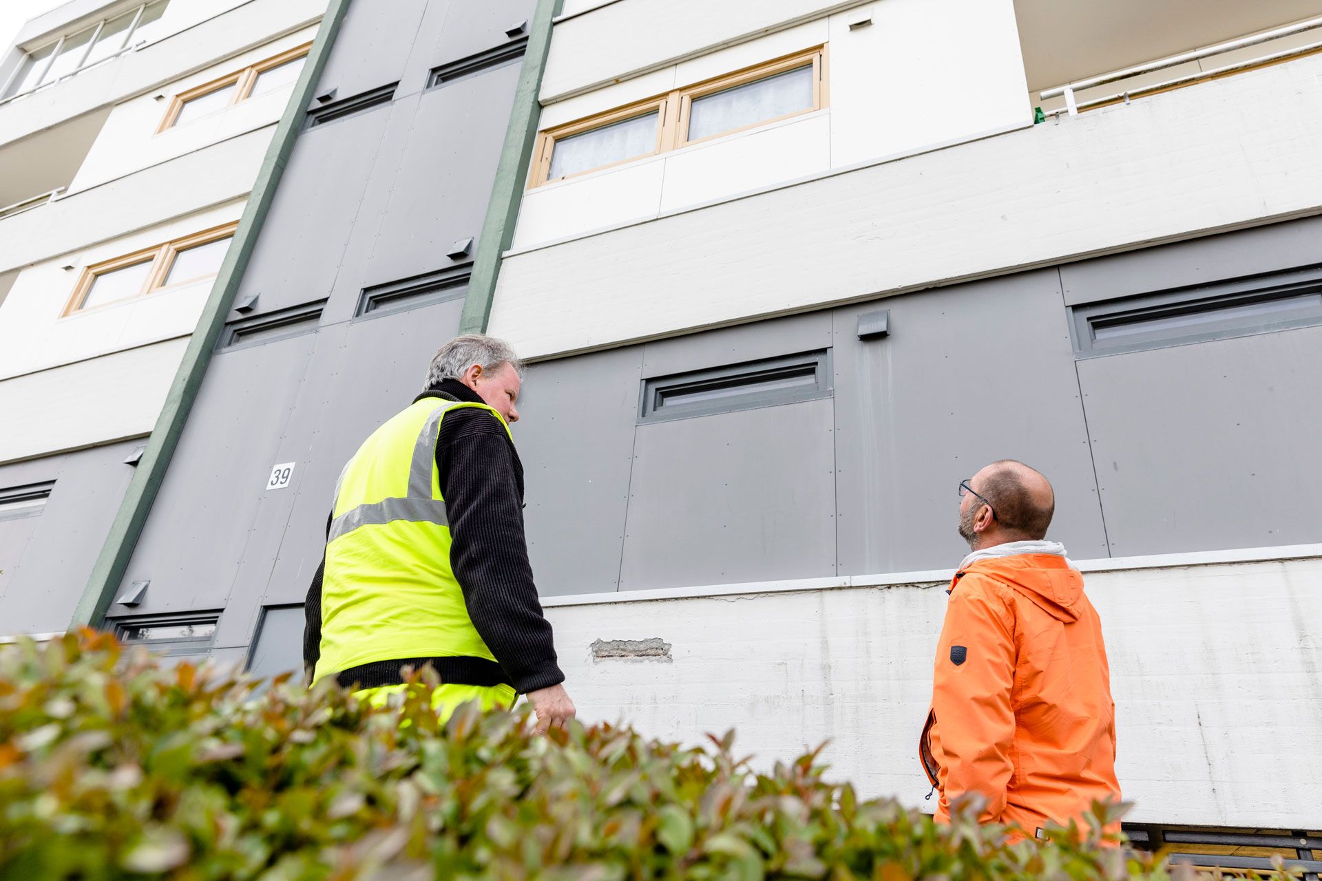 Menn kikker opp på betongfasade