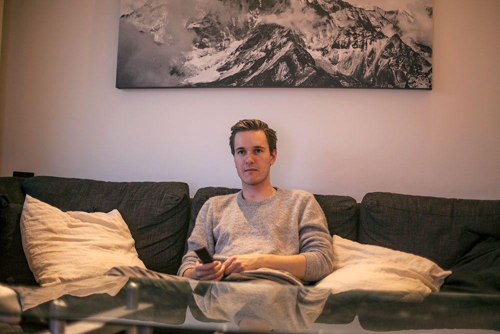 Simen Viste holder sitter i sofaen med fjernkontroll i hånda