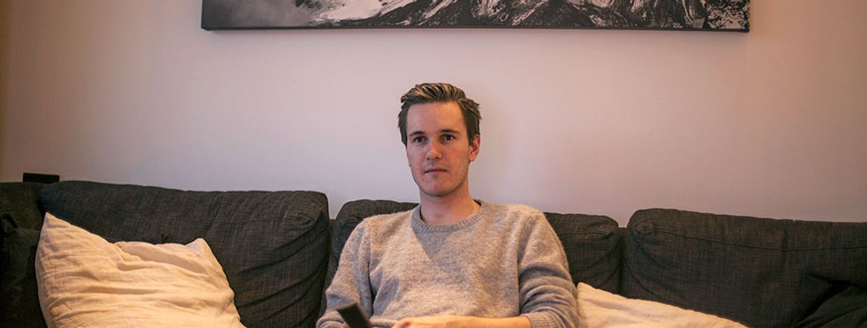 Simen Viste holder sitter i sofaen med fjernkontroll i hånda