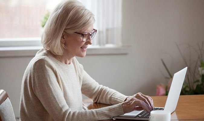 Eldre kvinne sitter foran bærbar pc