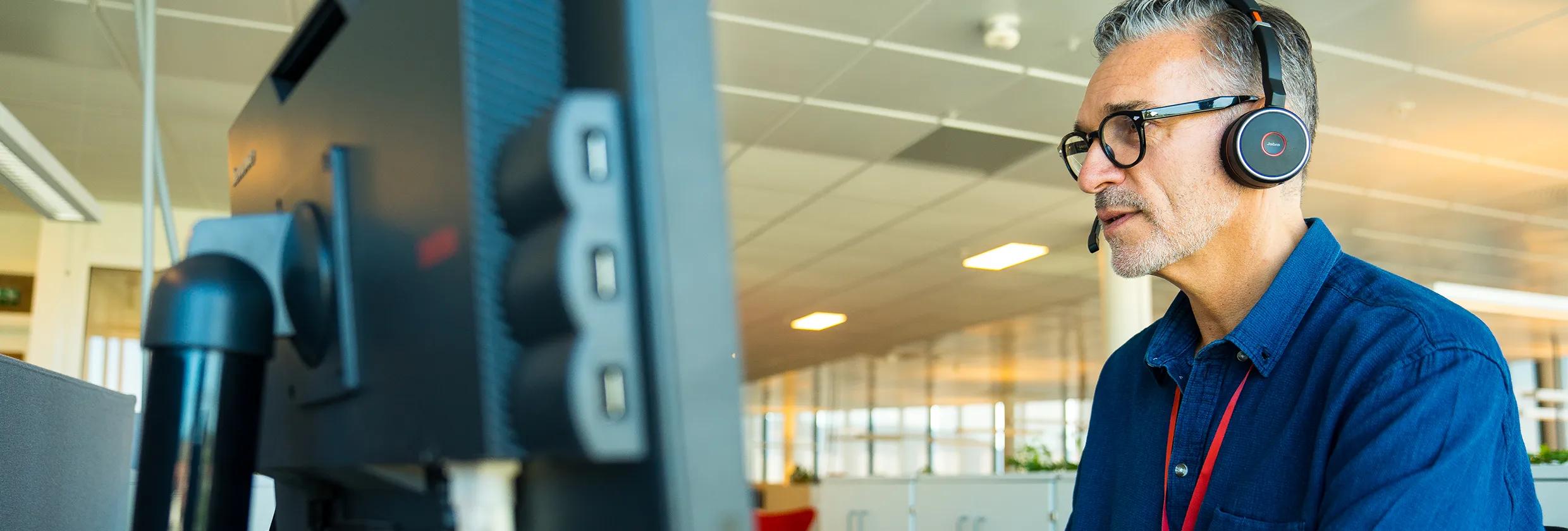 Bate-ansatt med hodetelefoner arbeider på en pc