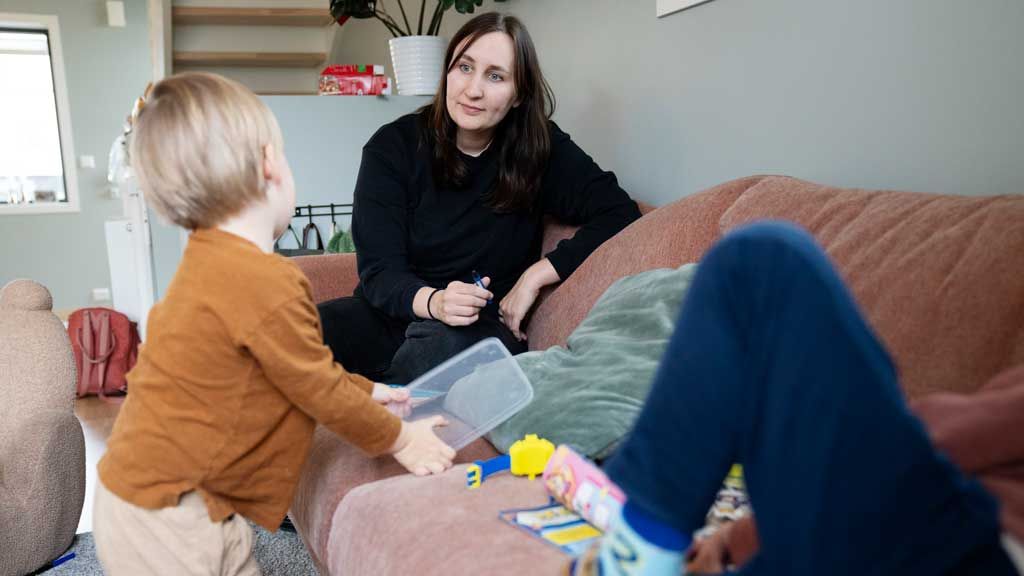 Ung mor med to barn som leker ved sofaen