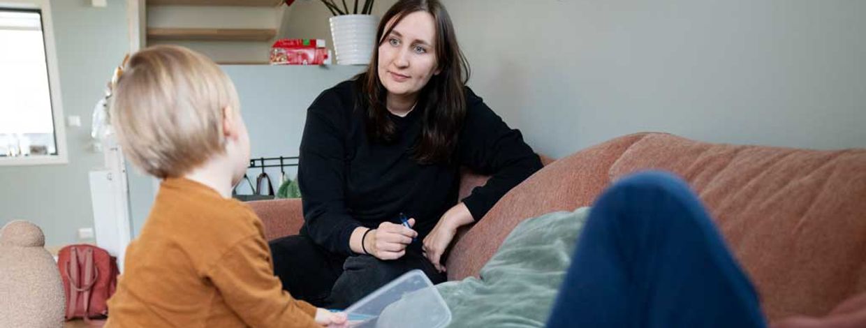 Ung mor med to barn som leker ved sofaen