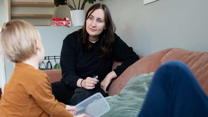 Ung mor med to barn som leker ved sofaen