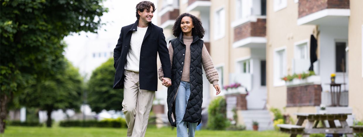 mann og dame hånd i hånd på plenen foran boligblokk