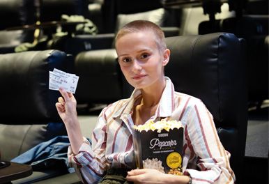 jente i kinosal med kinobilletter og popcorn