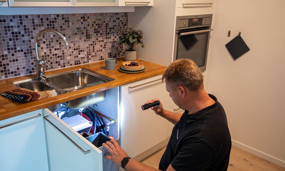 Takstmann sjekker under kjøkkenvasken
