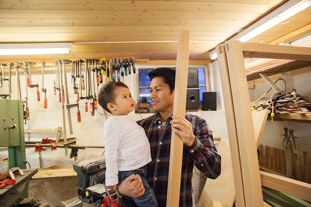 Far Daniel med sønn Emilian på armen i snekkerverkstedet