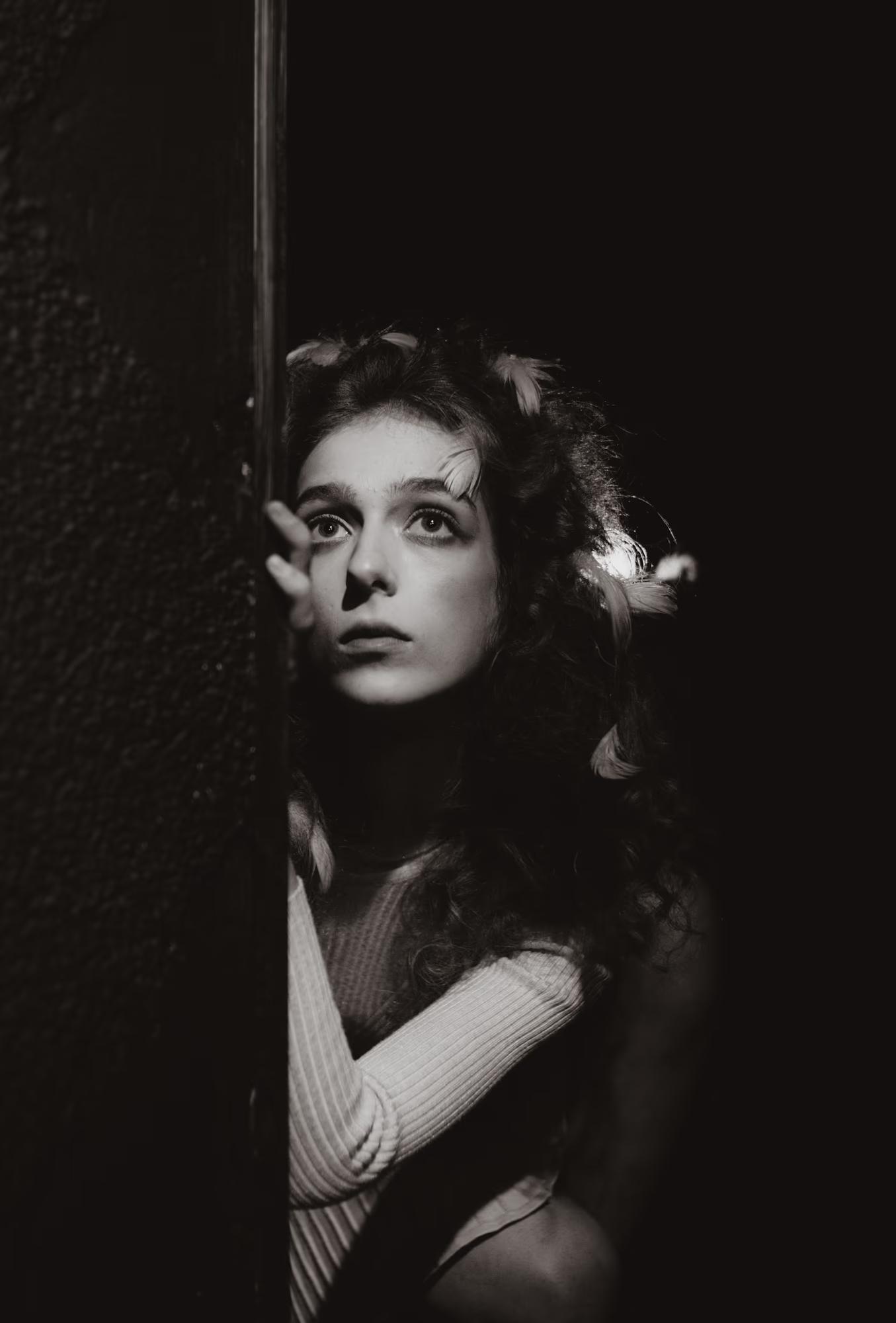 Low-key black and white style portrait of a model peeking through stage drapes.