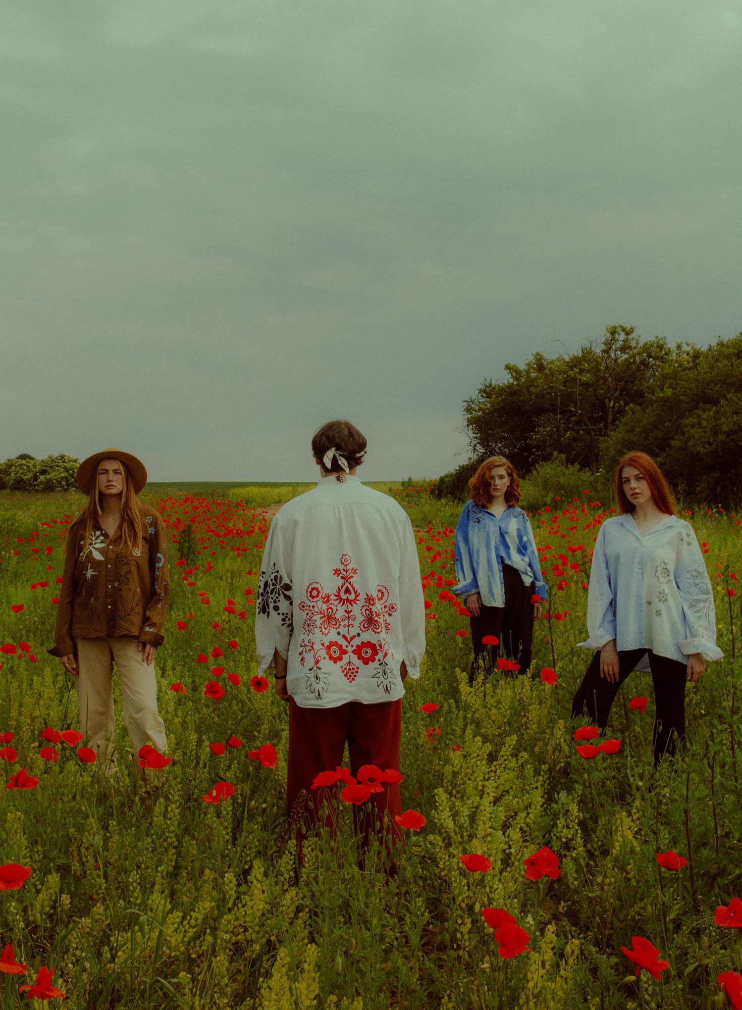 Full body fashion campaign wide shot of group of women in Ukrainian designer ethnic outfits walking through green poppy field, Ukraine countryside editorial