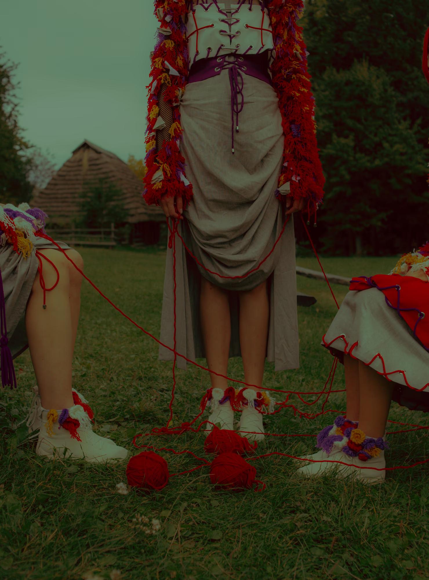 Focus on footwear and the hem of a traditional skirt decorated with red flowers, shot on a grassy path in a rural village setting.