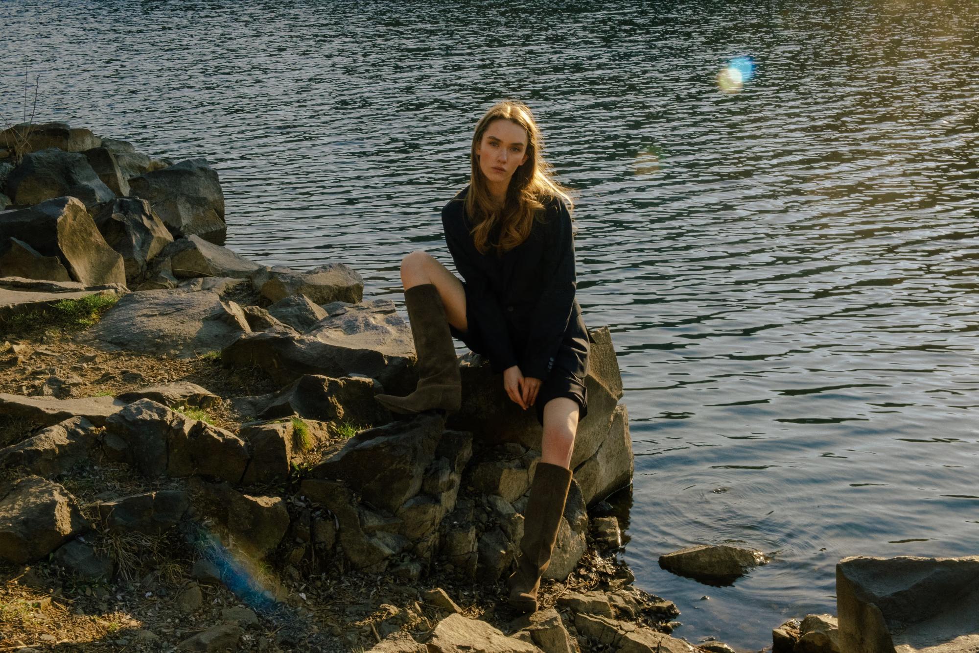Side-profile portrait: The model leans slightly, facing the water, her hair caught in a gentle breeze by the lake.