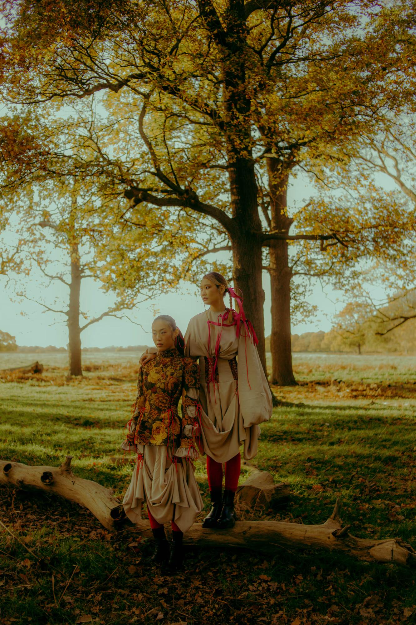 Full body fashion campaign shot of woman in designer floral outfit standing by large oak tree in golden afternoon light, Richmond Park London