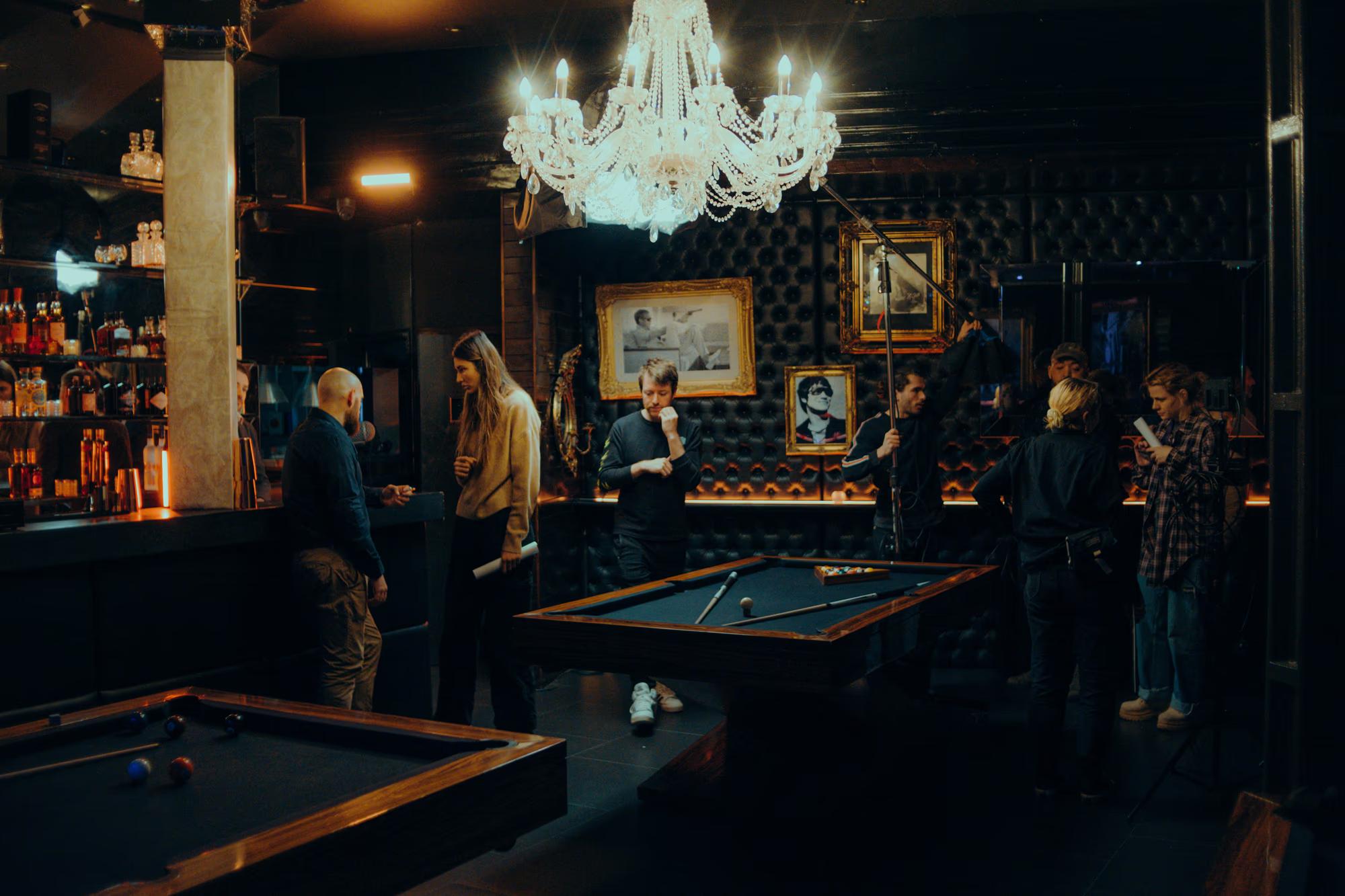 Wide view of a movie set inside a traditional pub, showing the director and crew during a production break.