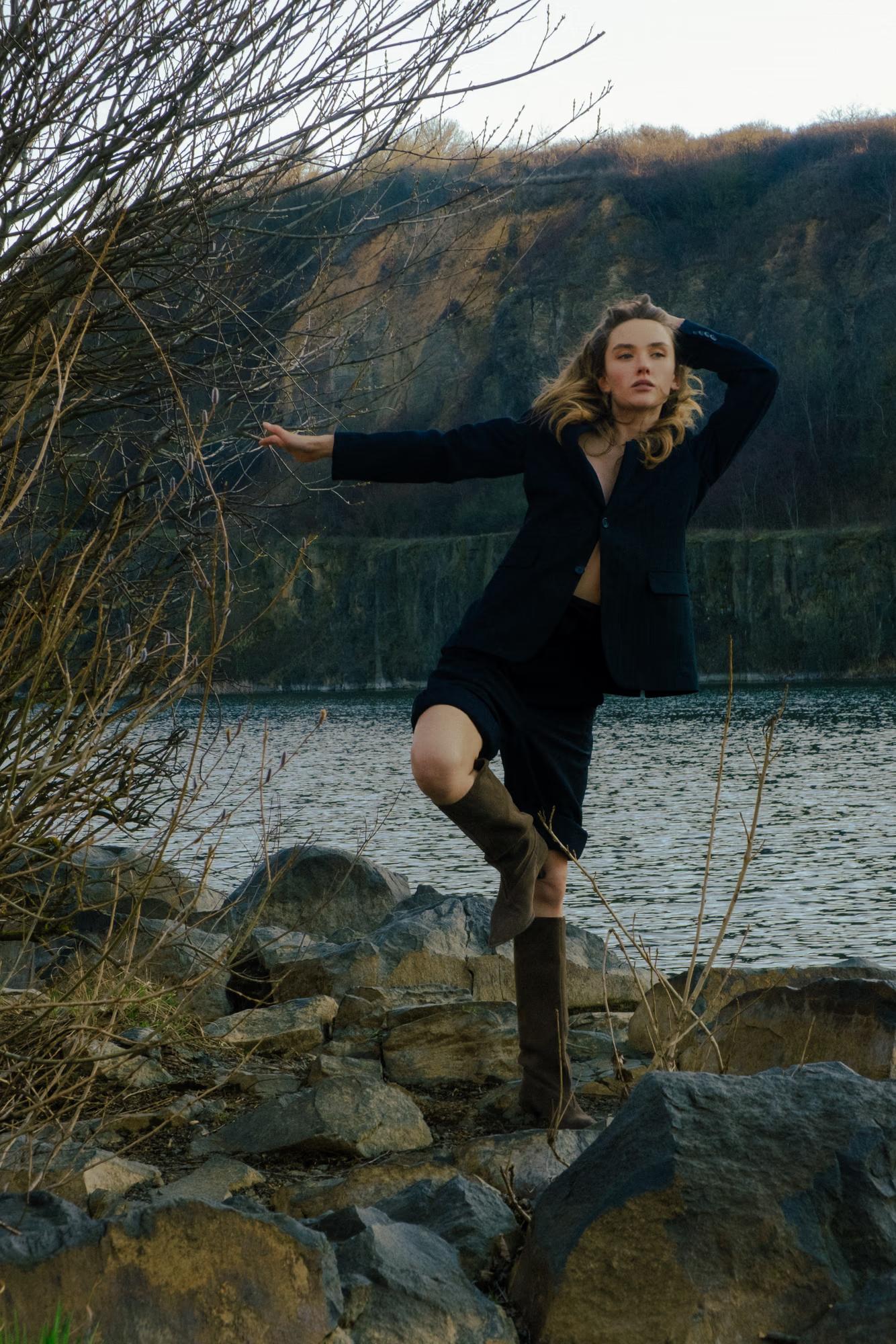 Direct view: The model stands confidently on the lake shore rocks, blending natural beauty with modern fashion aesthetics.