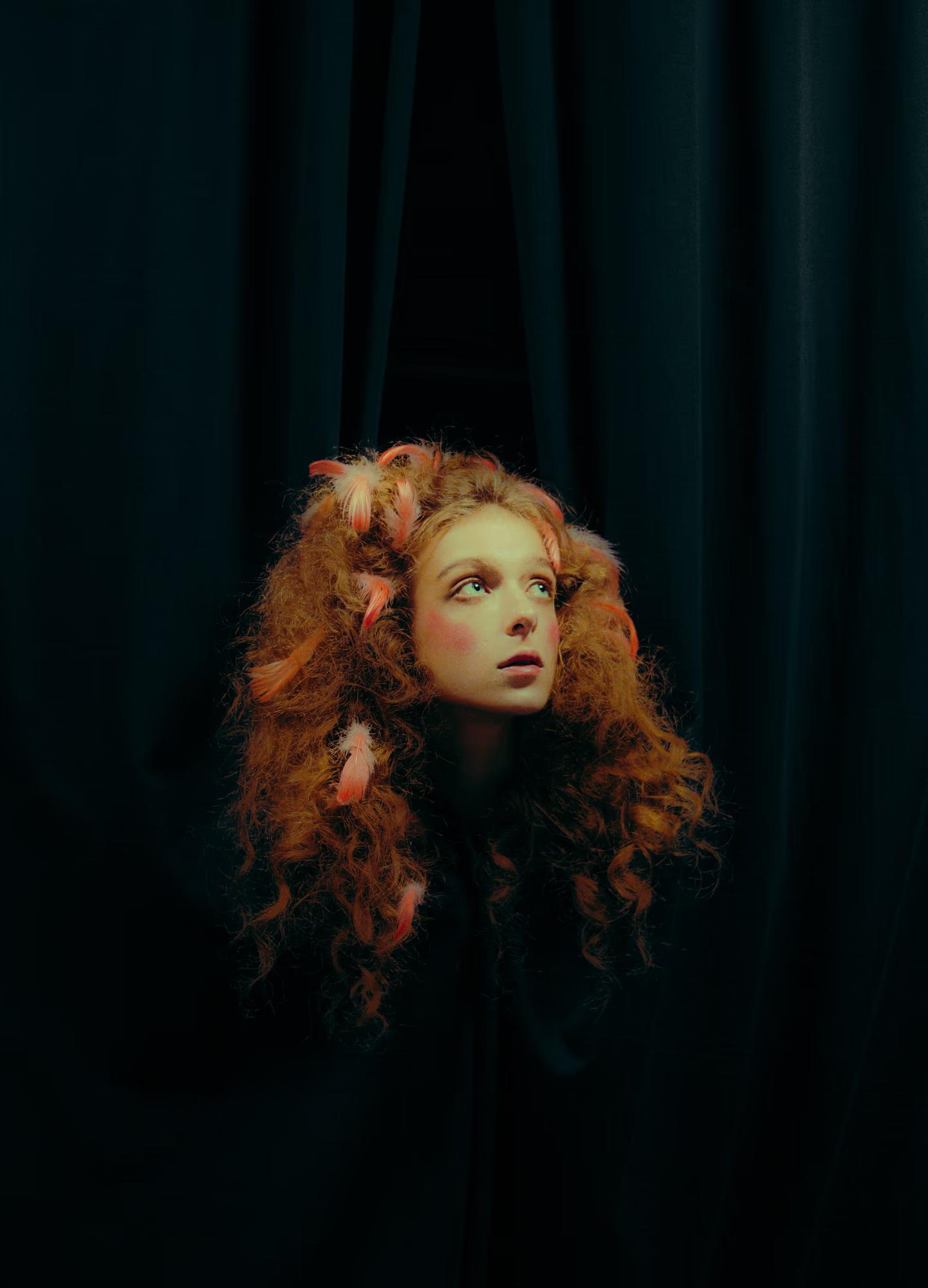 Dramatic lighting portrait of a redhead woman against a dark theatrical backdrop.
