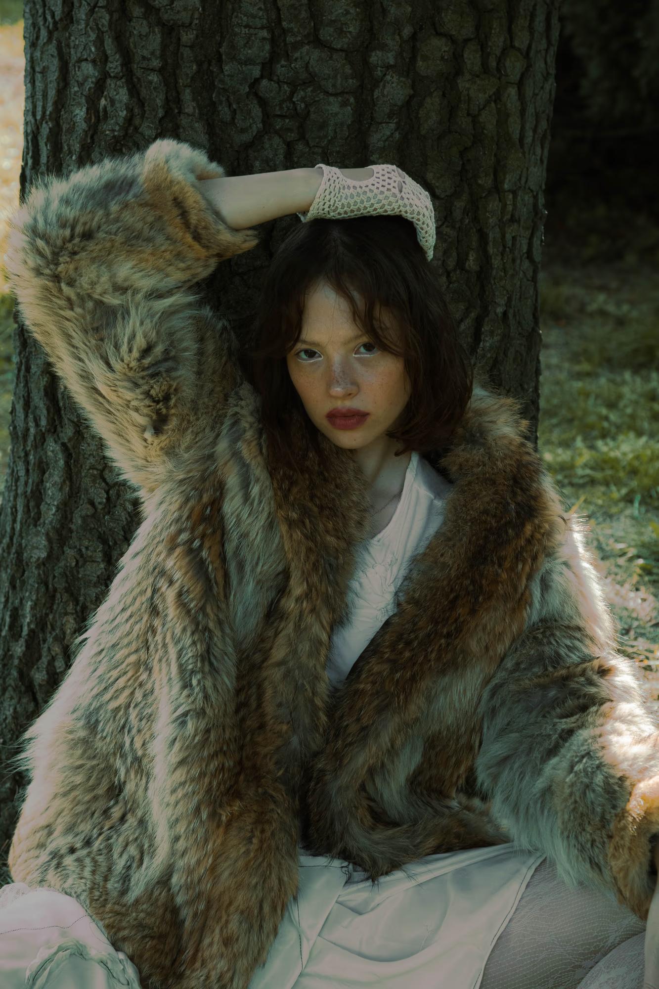 Medium fashion art portrait of woman in fur coat with arm raised, dark moody forest background, sensual dark fantasy editorial