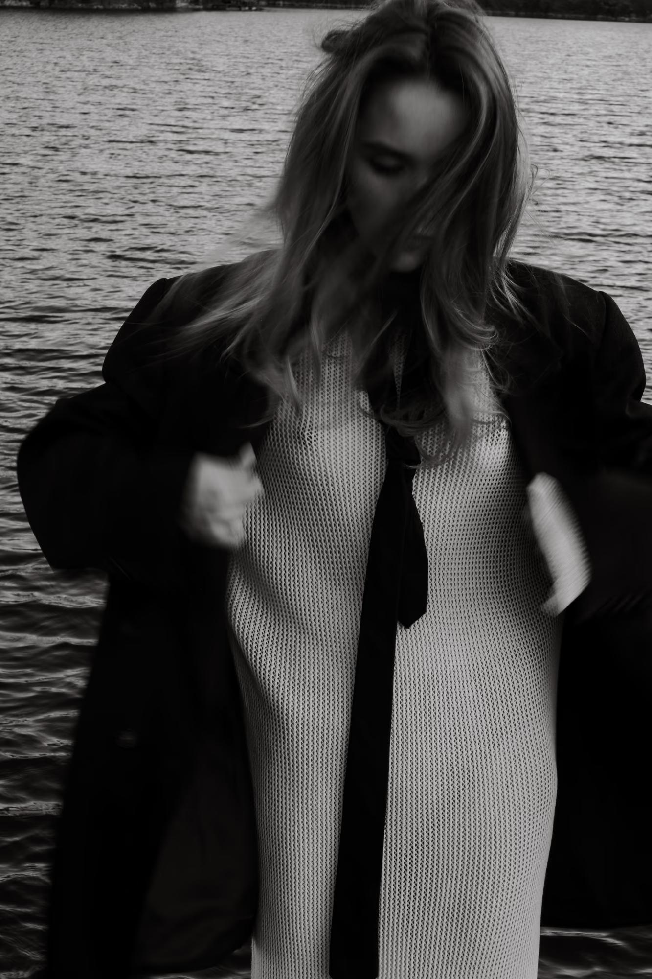 Black and white detail shot of the model's profile, with soft light reflecting off the lake in the background.
