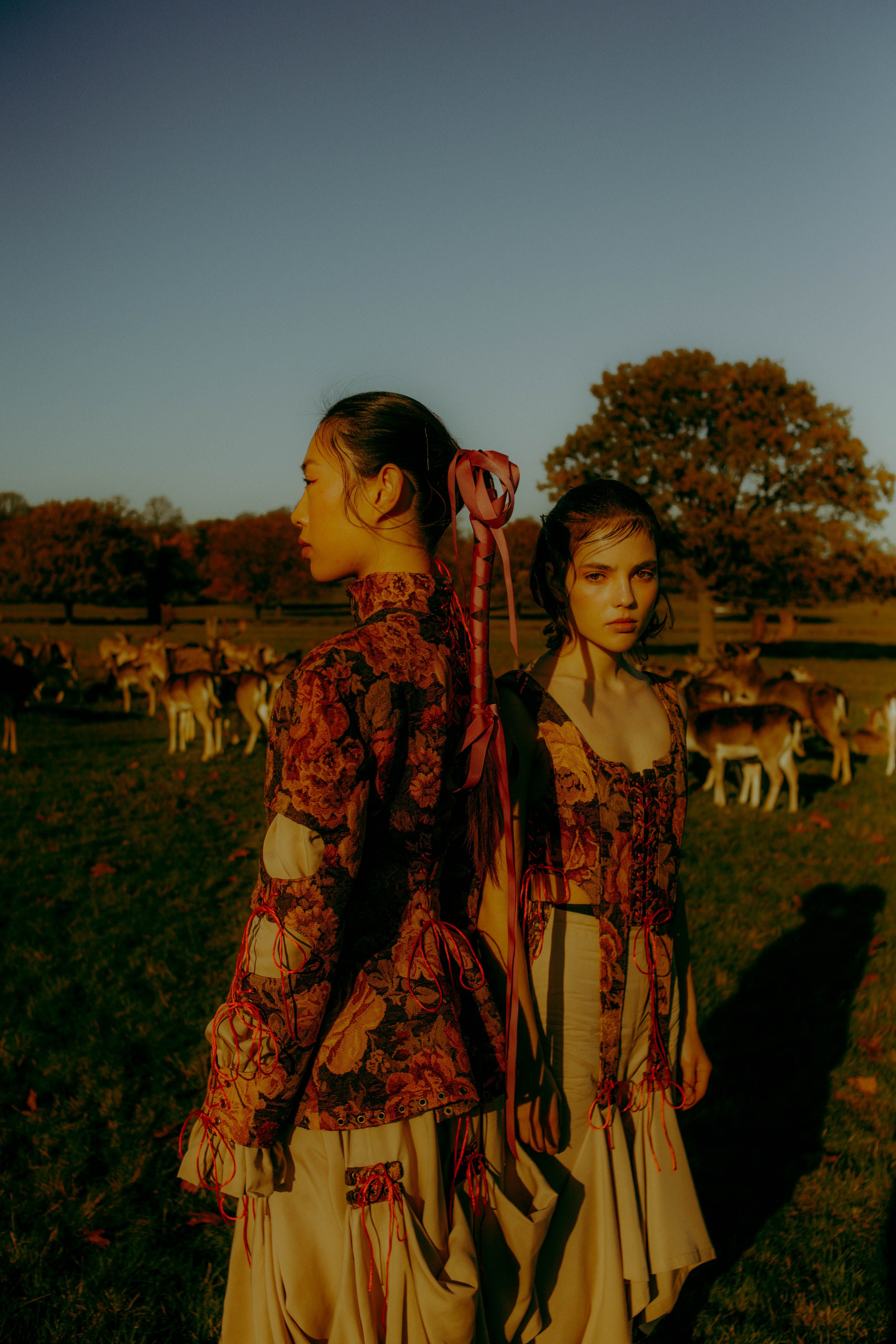 Full body fashion campaign shot of woman in bold floral designer dress in Richmond Park London, warm golden hour light, luxury editorial