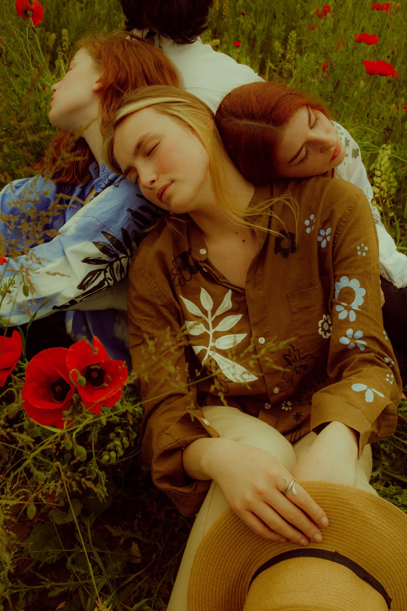 Medium fashion campaign shot of two women in Ukrainian designer outfits embracing among red poppies, intimate editorial, Ukraine field