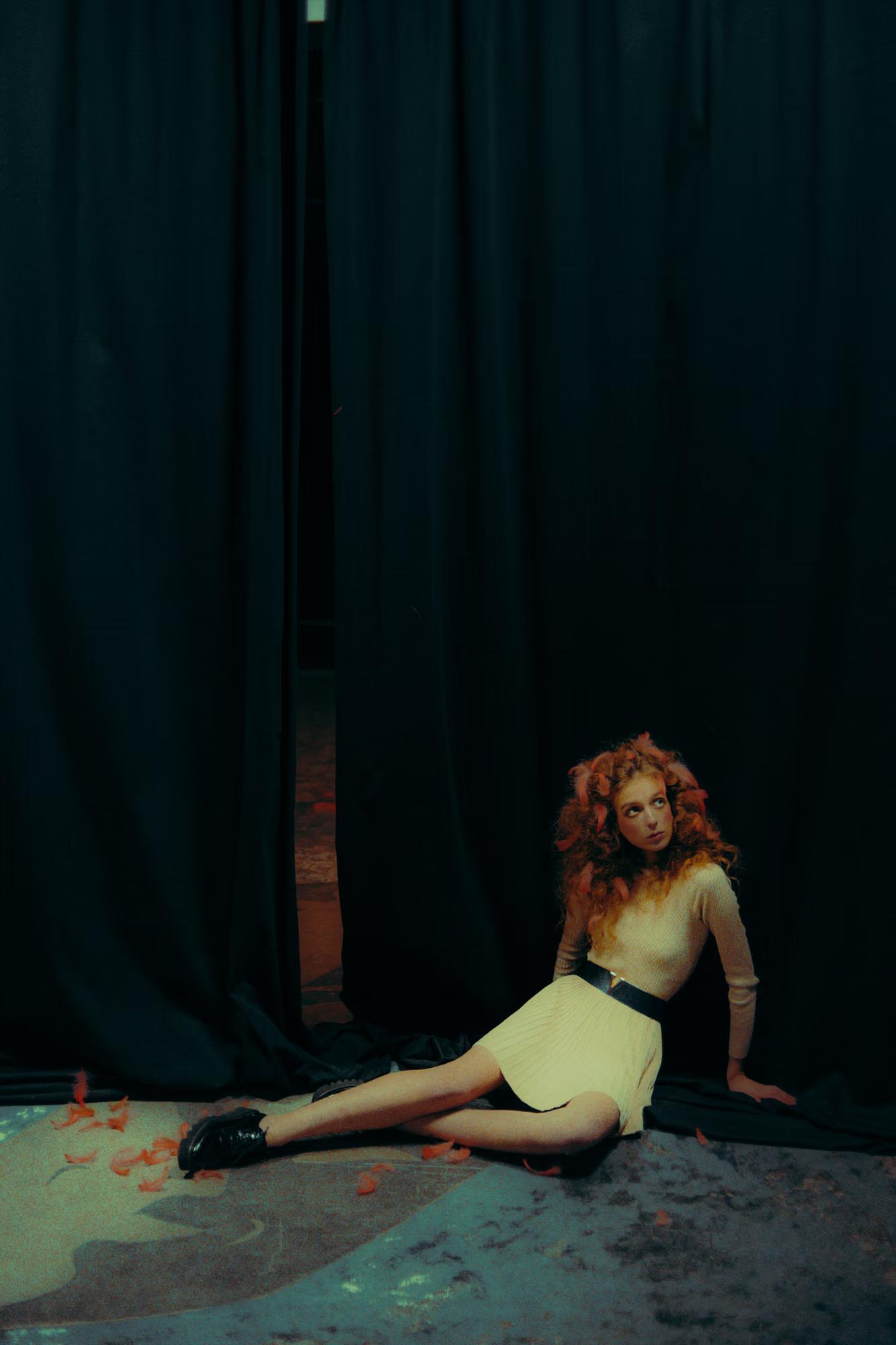 Wide shot of a model sitting on a theater stage floor, minimalist artistic fashion composition.