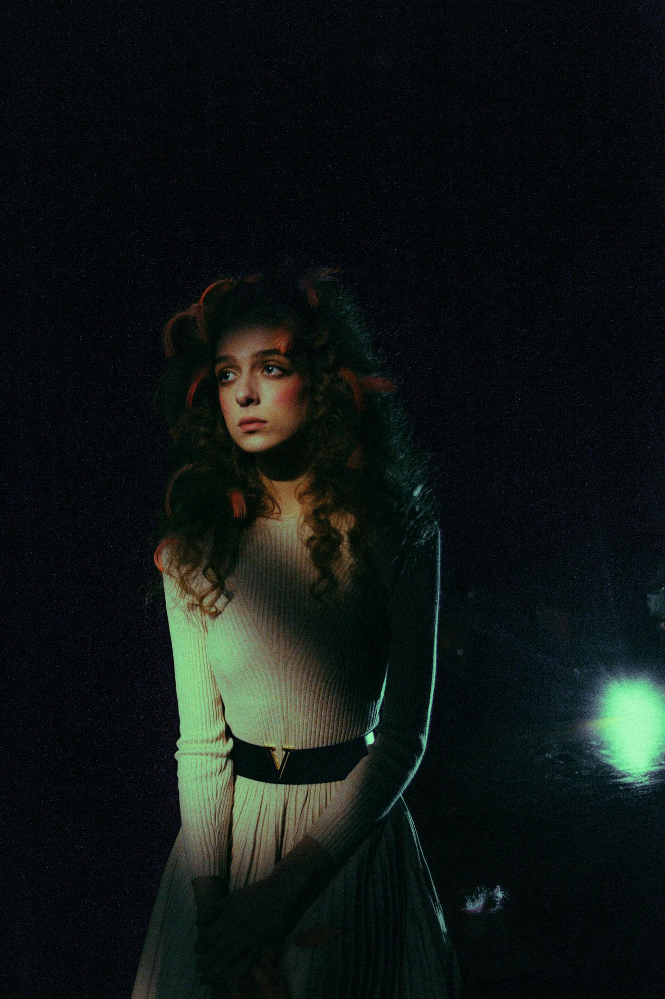 Cinematographic portrait of a woman in a white dress on a theater stage with spotlight.