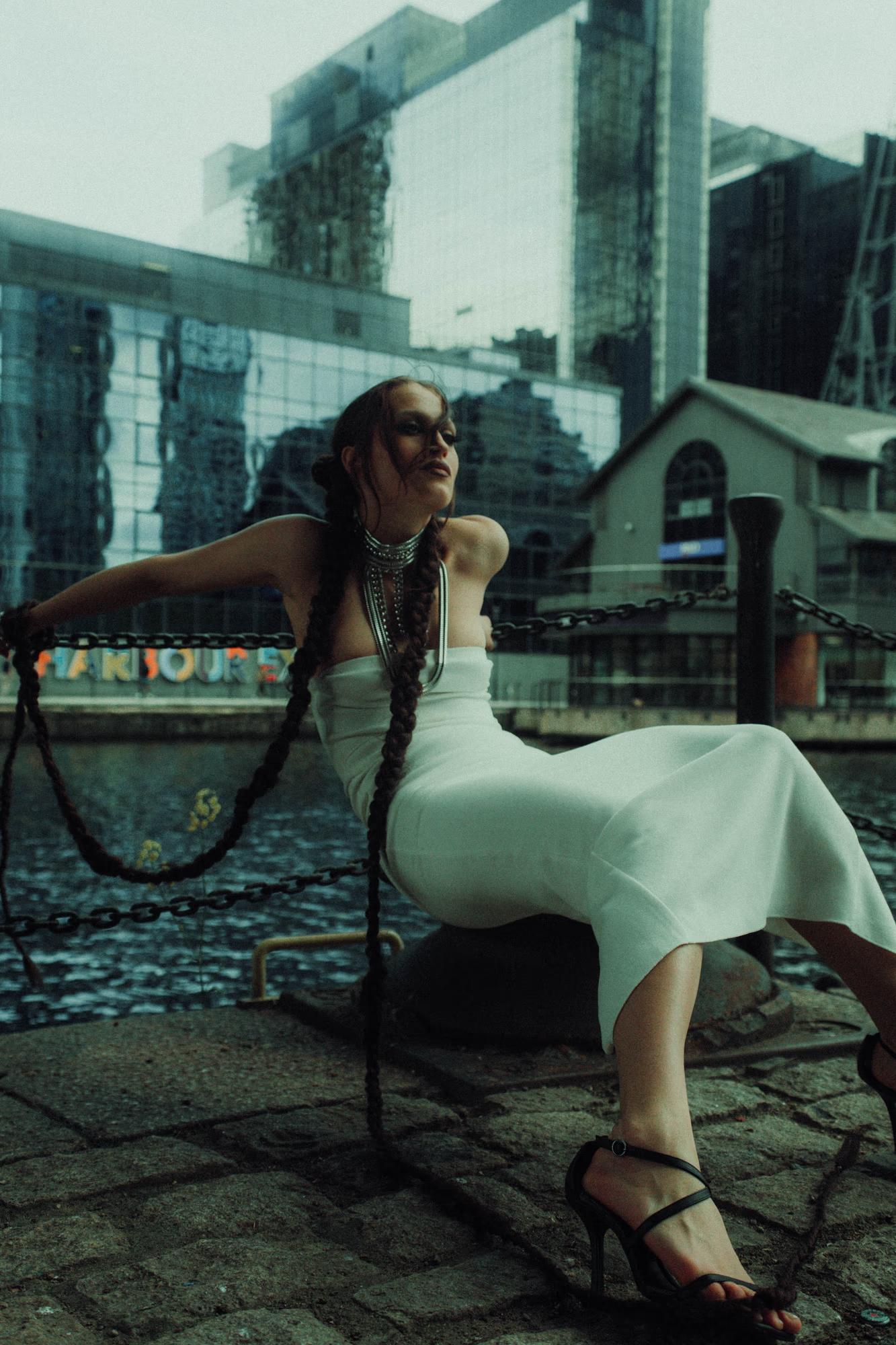 Medium shot of woman standing near water with teal-toned glass skyscrapers in background, Canary Wharf London docklands