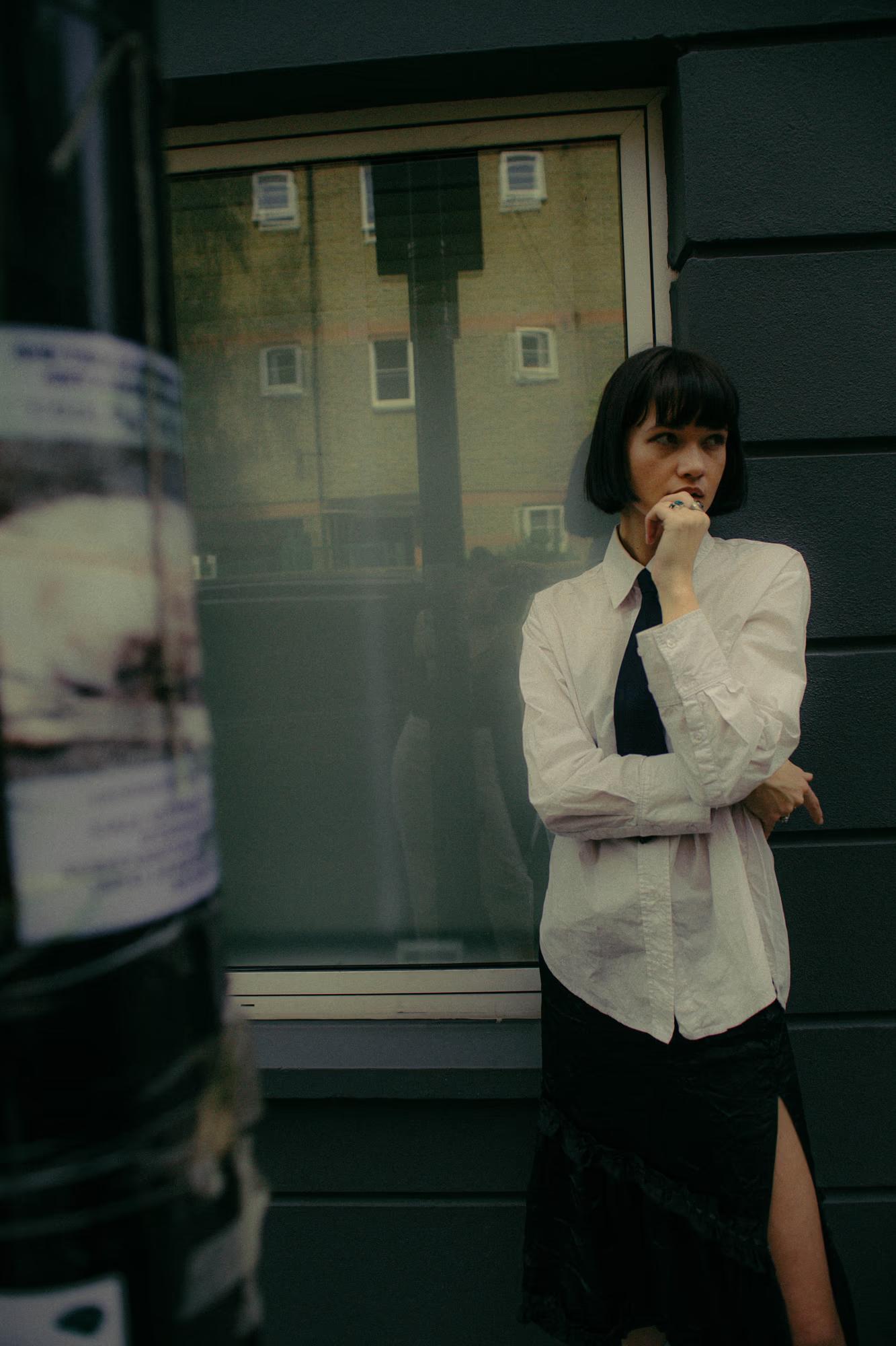 Full body fashion shot of woman in white shirt and tailored dark trousers against shopfront window, Shoreditch London urban editorial