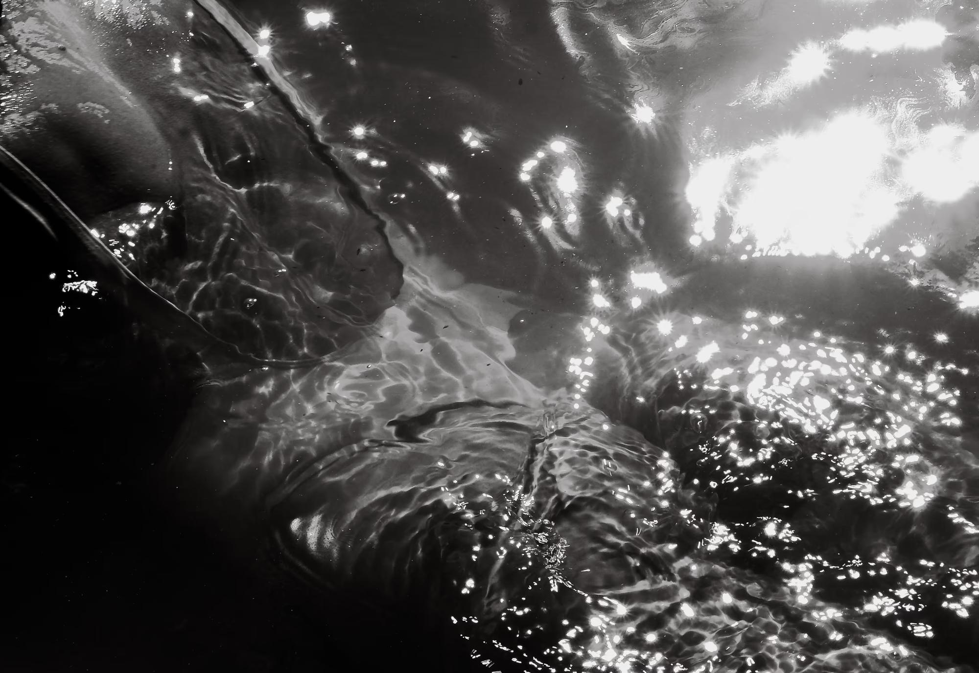 Dynamic underwater black and white shot of woman breaking through water surface with dramatic splash and sunlight burst, high contrast fine art photography