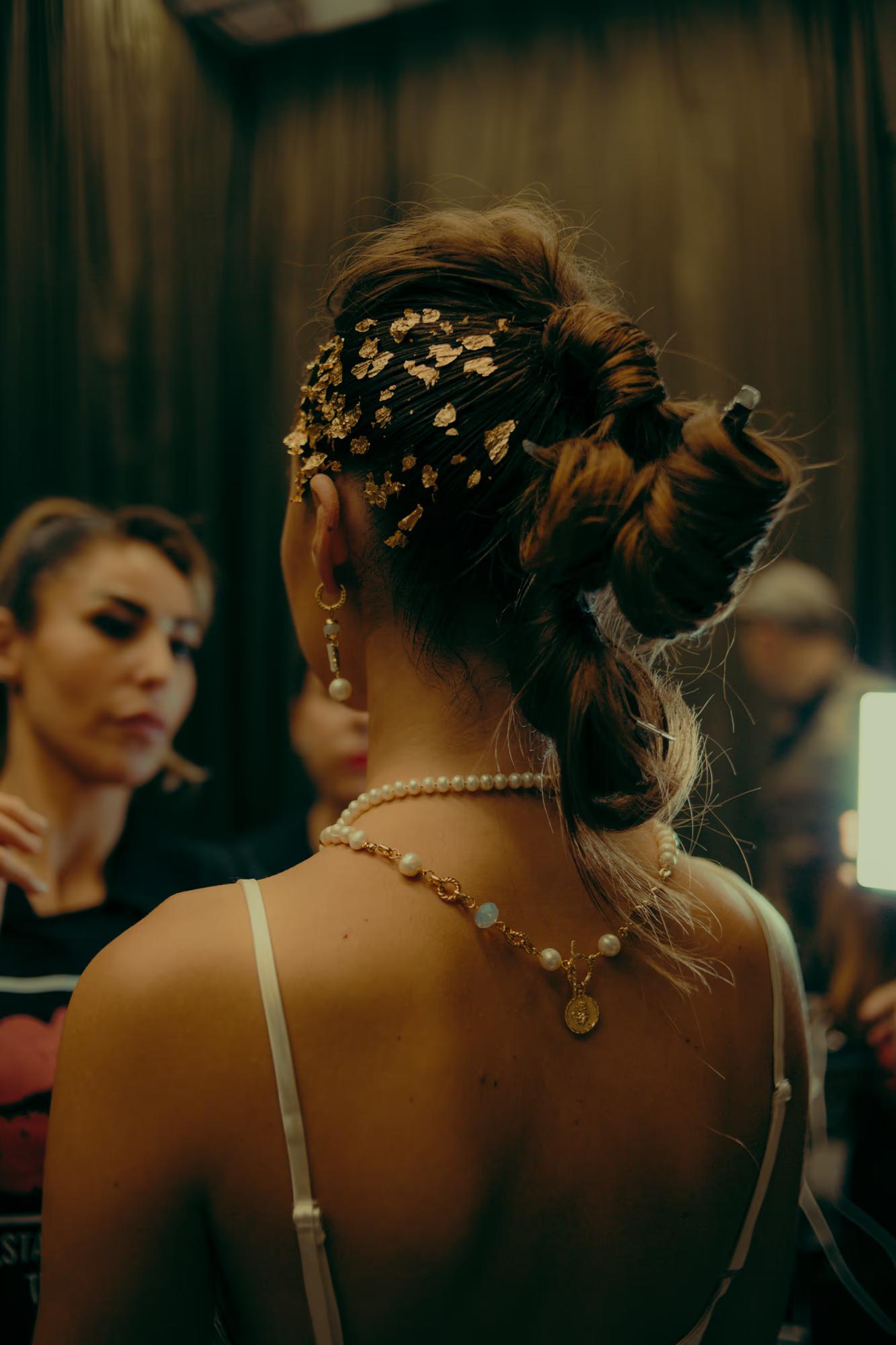 Close-up of an intricate hairstyle and back detail of a designer garment, captured during a fashion week backstage session.