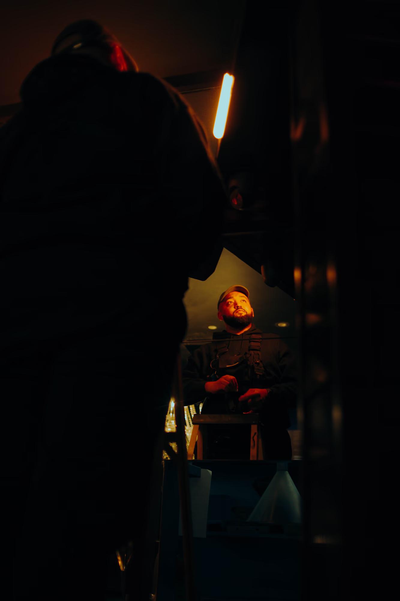 Low-key lighting shot of a cinematographer framing a dramatic moment on a dark London film set.