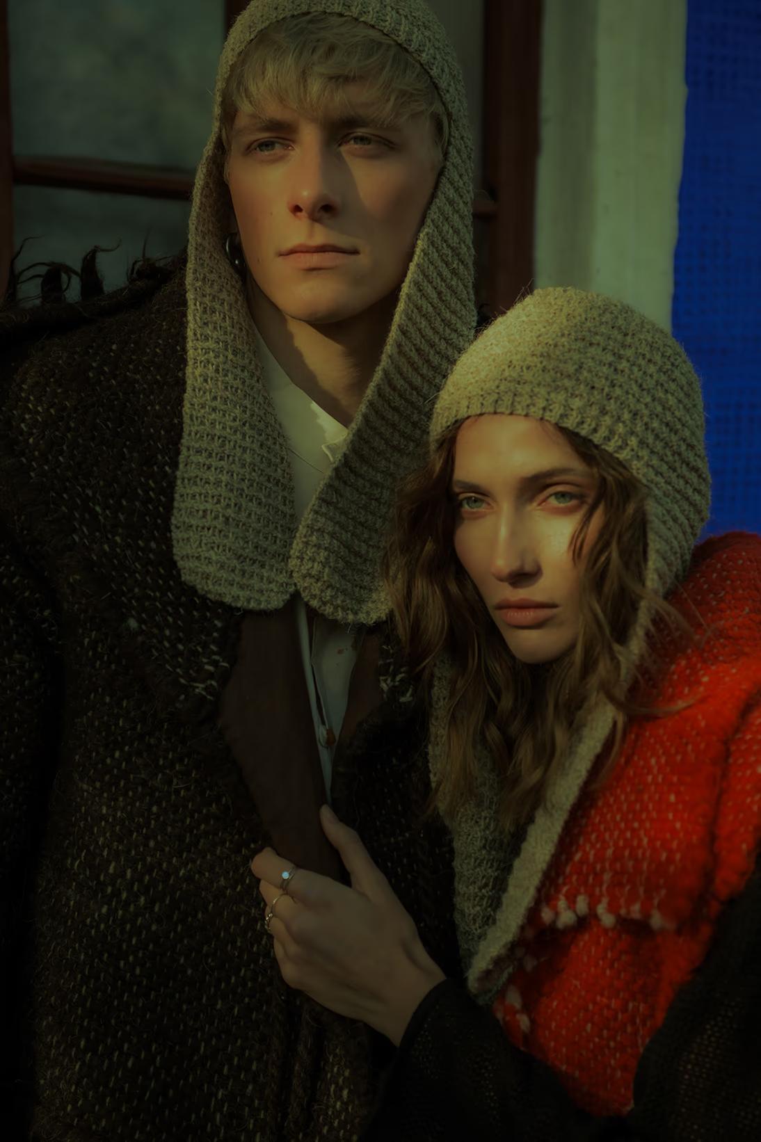 High-fashion portrait featuring models in Nordic-inspired woolens and hoods against a rustic Ukrainian village backdrop in Pirogovo.