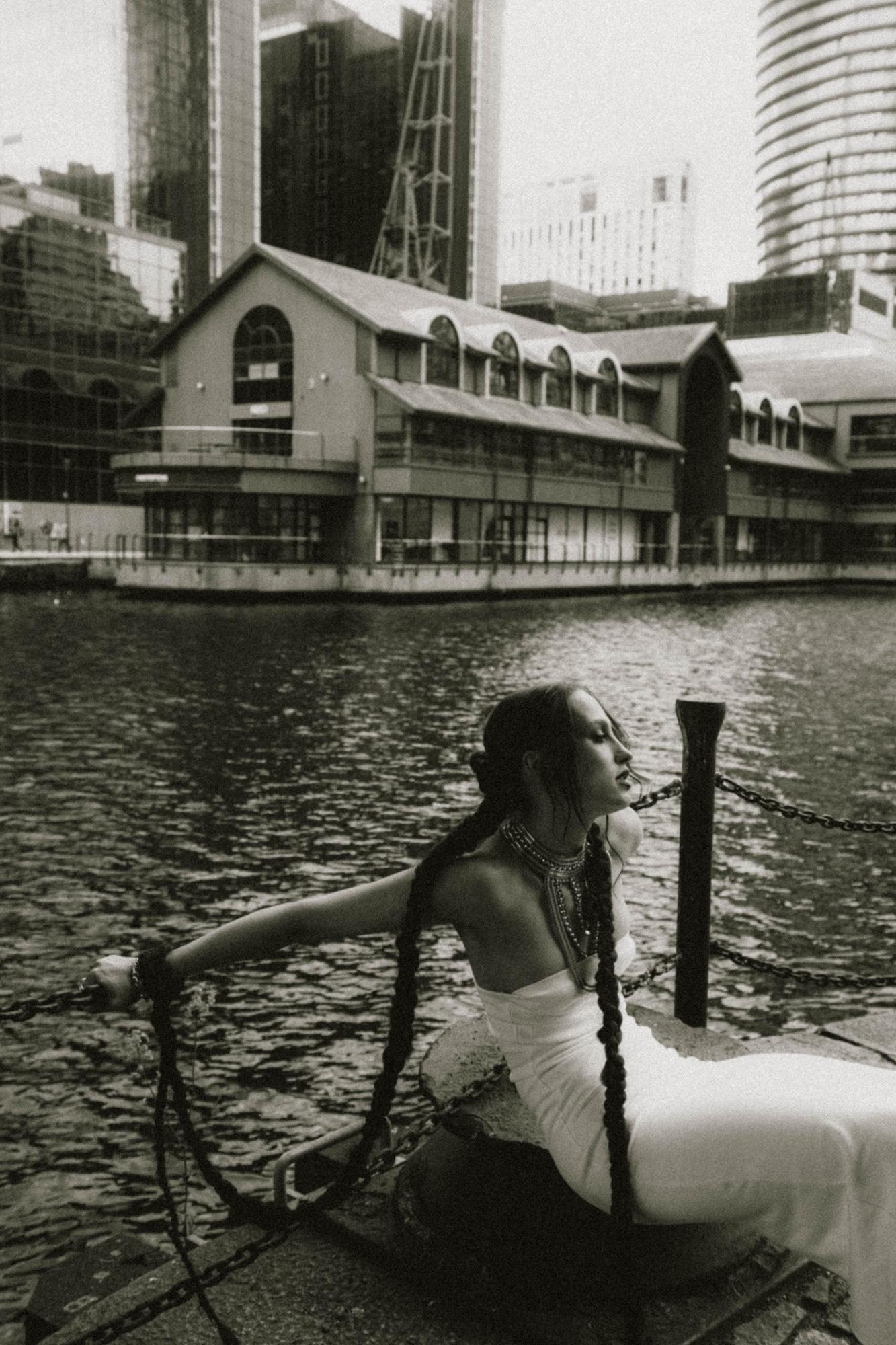 Wide establishing shot of female model near bridge or dock structure, black and white, Canary Wharf London
