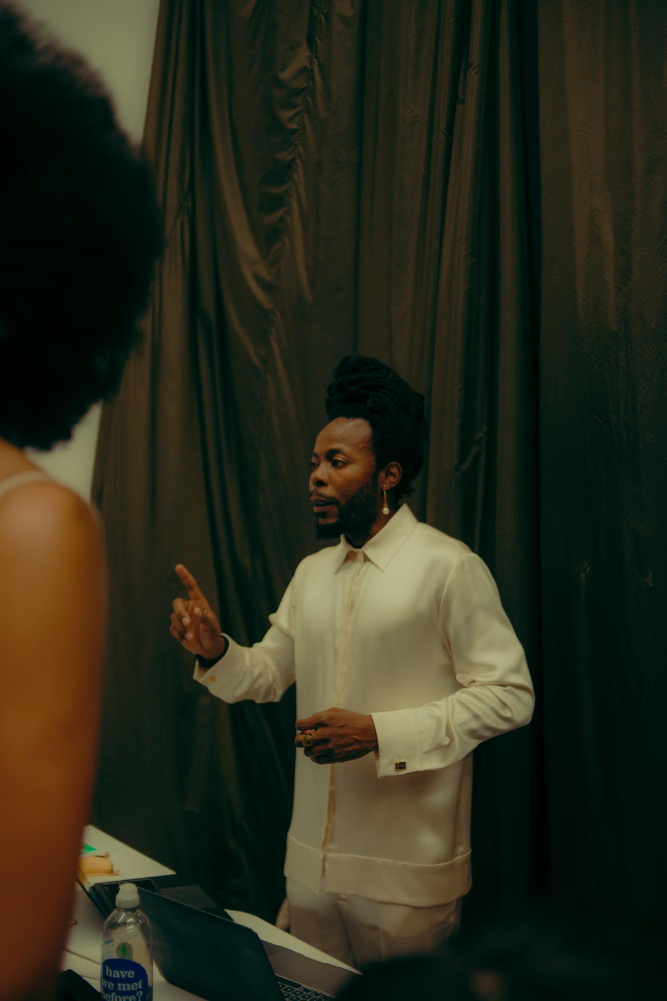 Model in a crisp white shirt having a conversation with the creative team backstage during runway rehearsals.