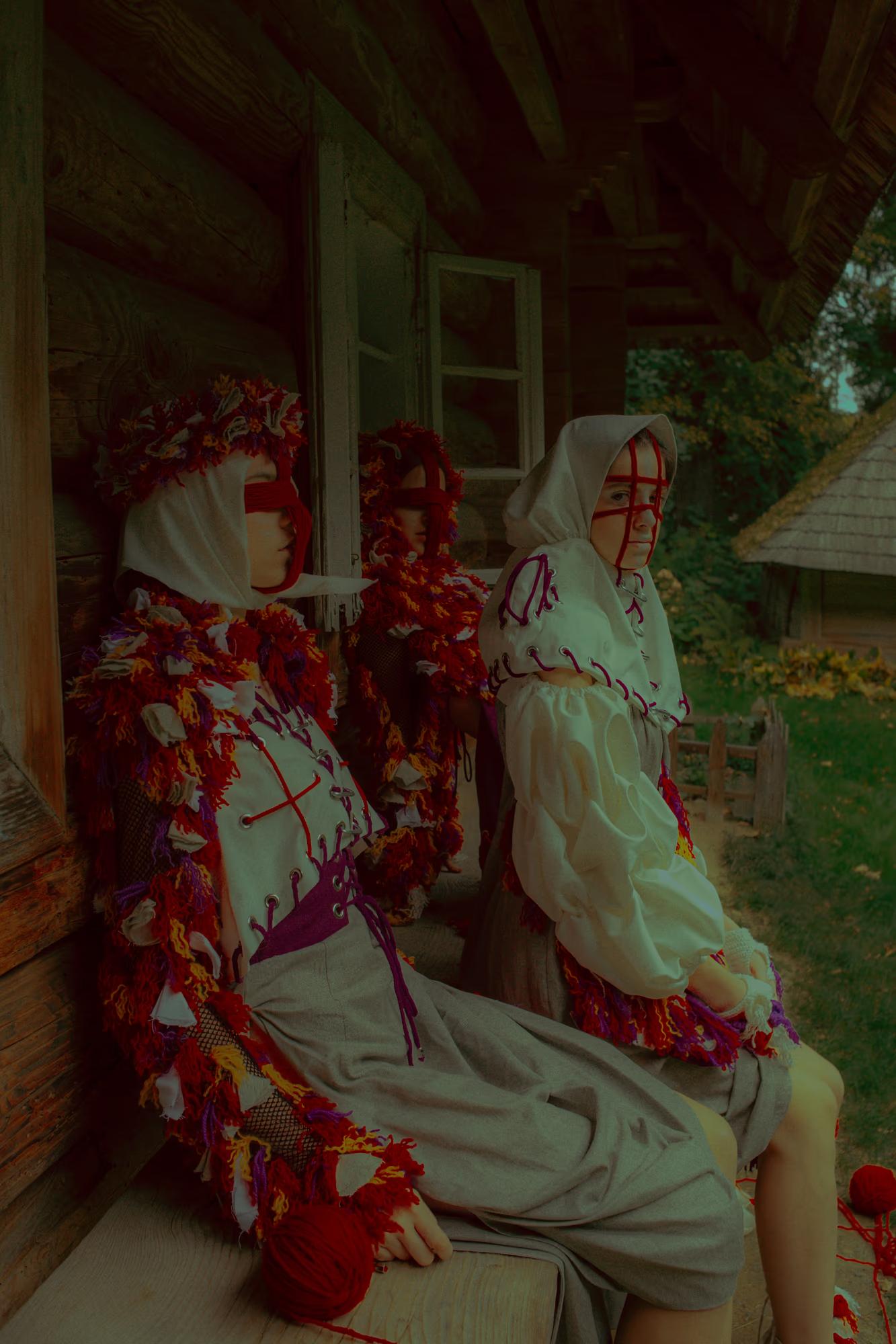 High-fashion pose: a model in stylized ethnic attire leaning against the dark logs of a traditional Lviv wooden cabin.