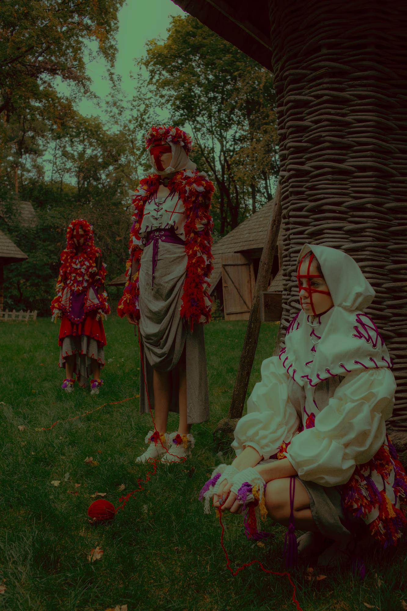 Candid-style ethno-fashion shot of models resting near a historic wooden fence, surrounded by the greenery of the Lviv ethno-park.