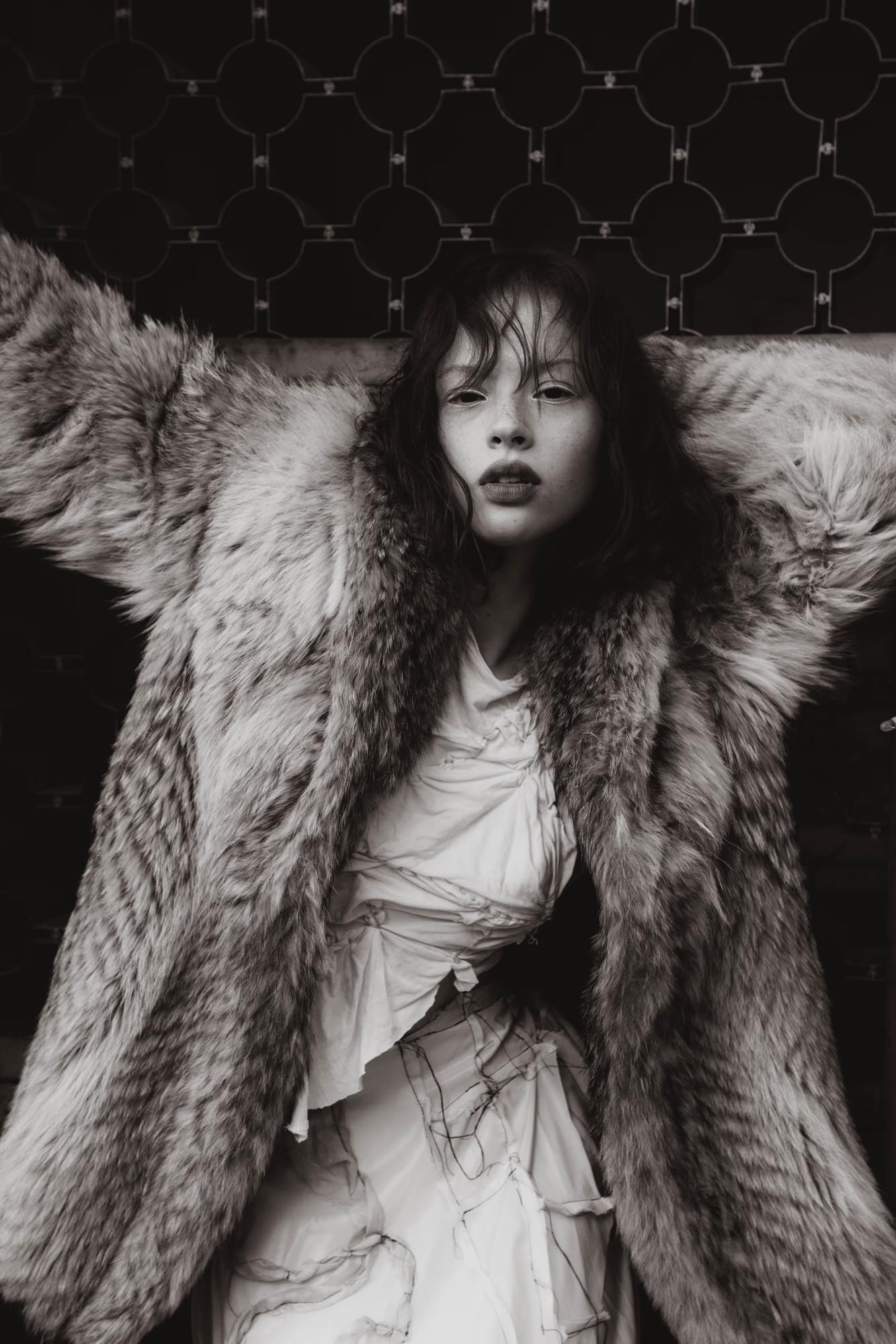 Medium fashion art black and white shot of woman in dark fur coat with wild disheveled hair, dramatic moody forest background, dark fantasy editorial