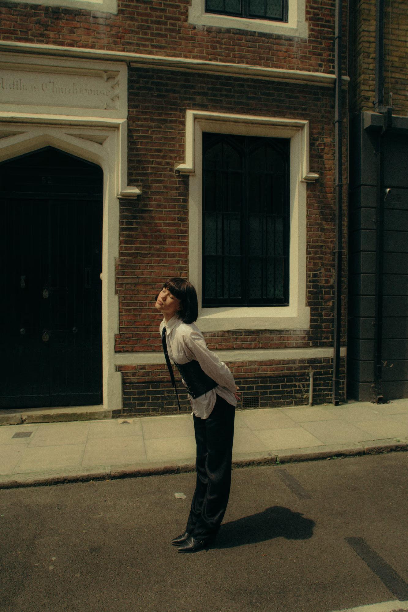 Full body fashion shot of woman in white shirt and dark trousers walking on Shoreditch London pavement, clean urban street style editorial