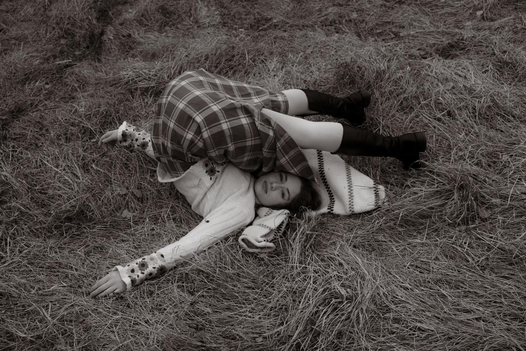 Black and white artistic overhead shot of woman lying in dry grass in Carpathian meadow, dramatic fine art ethno editorial