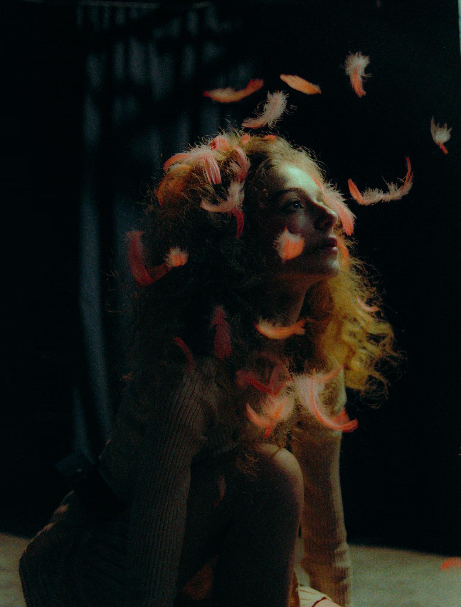 Close-up portrait of a redhead model with voluminous hair in a dark, moody theatrical setting.